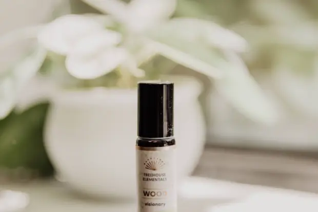 small-bottle-of-Treehouse-Elementals-Wood-essential-oil-blend-stands-on-a-windowsill-with-lush-green-plants-in-the-background